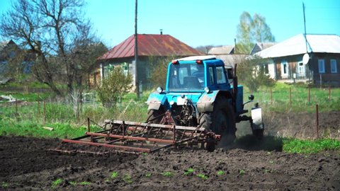 The tractor cultivates and cuts furrows in the field. Tractor work in the black soil field in the village
