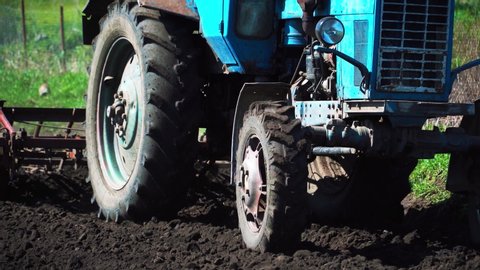 The tractor cultivates and cuts furrows in the field. Tractor work in the black soil field in the village