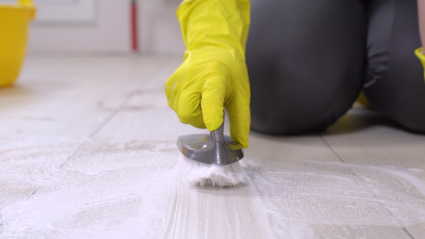 Woman in yellow rubber gloves with plastic basin with water, foaming detergent and brush cleans tiles on floor, front view, close up. Disinfection of surfaces, general cleaning of house | Shutterstock HD Video #1053733733