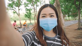 POV Portrait of joyful Asian girl wearing protective mask making video call online in green park smiling talking looking at camera waving hand. New normal life after COVID-19. Social Distancing.