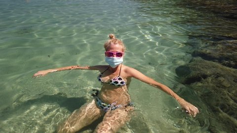 Italian girl swims in Fetovaia beach sea wearing medical mask during Covid-19. Blonde woman having a bath in Italian sea in Coronavirus quarantine. Holidays travel in COVID pandemic in Italy.