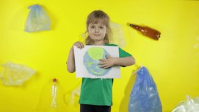 Child girl activist in green t-shirt with recycle logo holding painted with paints picture of Earth. Yellow background with cellophane bags, bottles. Save environment. Plastic trash nature pollution - Powered by Shutterstock - Get 15% off with code: PIKWIZARD15