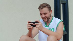 Basketball Fan Reaction Concept - Excited basketball player in basketball outfit watching his favourite team on smart phone, 4k slow motion