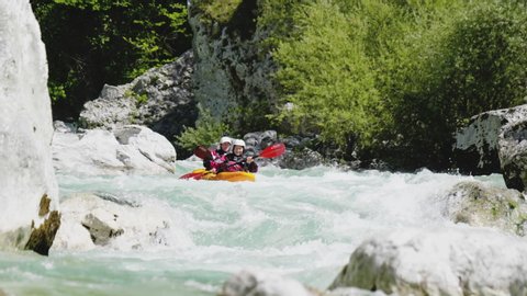 Slow motion close up two people kayaking in dual kayak on emerald whitewater river, over rapids, enjoying nature Soca, Slovenia