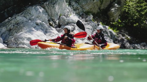 Slow motion close up two people kayaking in dual kayak on emerald whitewater river, over rapids, enjoying nature Soca, Slovenia