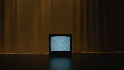 Old CRT TV is on the floor in a dark and empty room. On the screen there is a frightening white noise filling the room with a hypnotizing atmosphere of mystical evil. Dolly camera movement