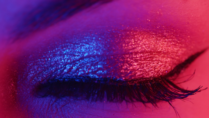 Extreme close up of human eye iris under neon light 4K. Female with beautiful makeup, glitter shadows and false lashes. Womens green eye contracting. Nightlife, night club concept. | Shutterstock HD Video #1053753182