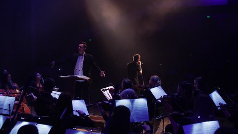 ODESSA, UKRAINE - DECEMBER 28, 2019: the conductor makes a gesture of hand movement to end the concert and the soloist spreads his hands for the audience from the scene, leaving for defocus