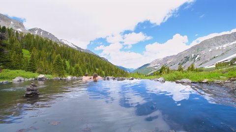 Woman and man couple swimming inside hot springs water looking at view on Conundrum Creek Trail in Aspen, Colorado in 2019 summer mountains