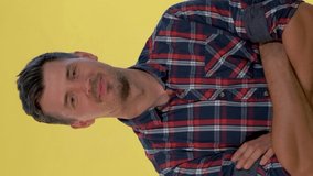 Happy young man bursting in laughter on yellow background. He is in checkered shirt. Video with Vertical Screen Orientation 9:16