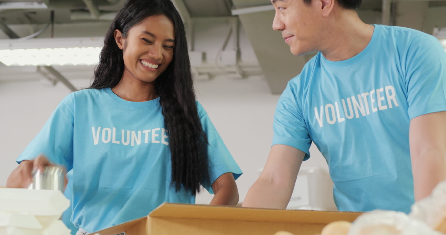 Male and female volunteer preparing free food delivery for poor people during covid19. As charity workers and members of the community work together filling boxes with food. Royalty-Free Stock Footage #1053762941