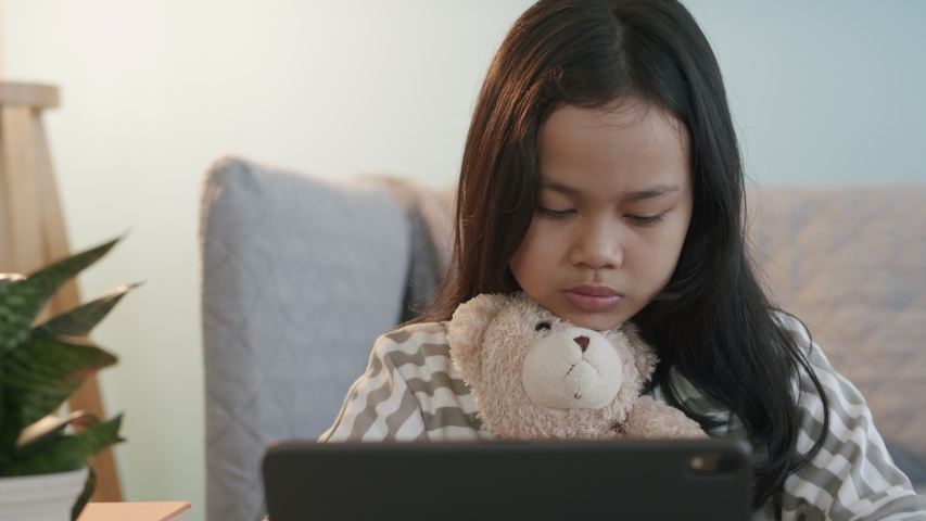 Asian little girl using a digital tablet while sitting at interior home night. hand of Asia child touch screen. Close- up on the face kid