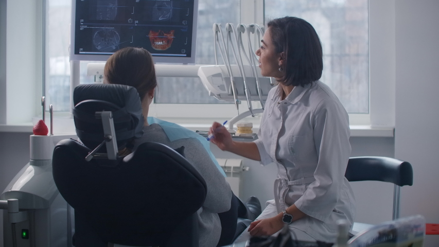 A female doctor discusses with the patient a plan for recovery and rehabilitation of the face after the accident looking at an x ray image on the monitor screen | Shutterstock HD Video #1053766961