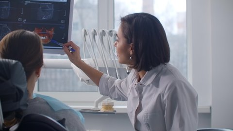A female dentist shows an MRI image on the screen and an x-ray of the patient's teeth. Discussion of the treatment plan and healthy smile. Recovery after an accident