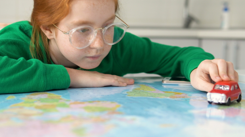 Little cute girl travel over world map by red car. Toy transport in child hand