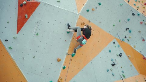 rock climber makes hard move on challenging route using heels, clipping rope to quickdraws. rear view strong girl climbing on overhanging rock wall on outdoor climbing center.