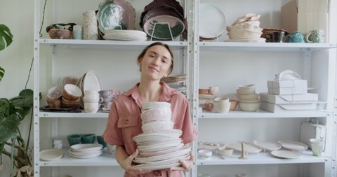 Portrait of a young smiling attractive female potter stay and holding clay bowls. Woman making ceramic item. Pottery working, handmade and creative skills