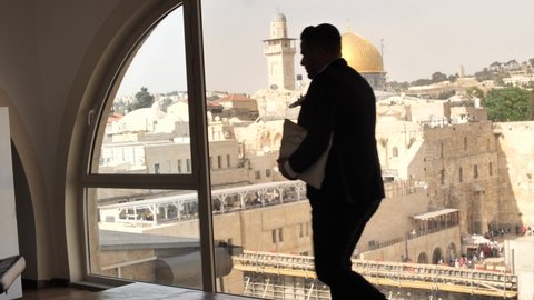 Jew with tallit bag walks across loft window with view on Jerusalem Temple Mount