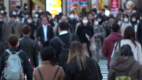 TOKYO, JAPAN - MAR 2020 : Crowd of people at the street near Shinjuku station in evening rush hour. Commuters and tourists wearing surgical mask to protect from Coronavirus (COVID-19). Slow motion.