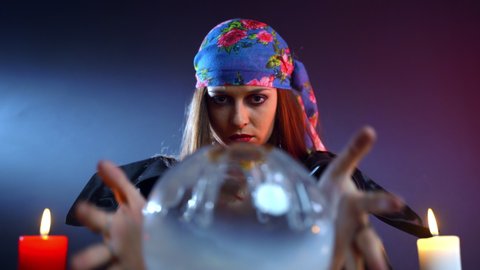 Female fortune teller moving hands above the magic crystal ball and spelling over it searching missing person, witch calling spirits to talk, person's fate in sorcerer's hands. Connection with