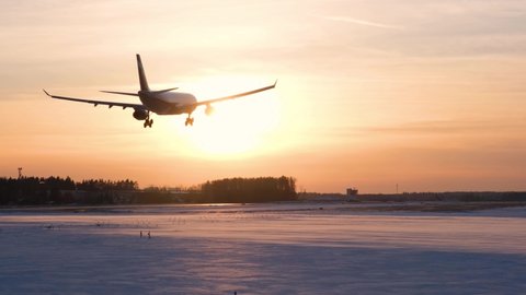 Silhouette of a passenger plane that lands at the airport at sunset in winter