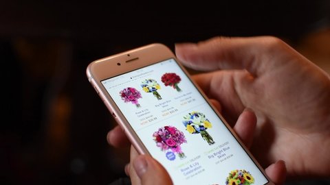 Moscow. Russia. May 2020. female hand with phone chooses bouquet of fresh flowers for home delivery. catalog of fresh flowers, delivery of bouquets. woman buys flowers in online store on Internet.