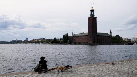 Bike rider sitting by waterbody in front of landmark town hall building in Stockholm