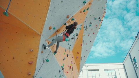 profile view strong girl climbing on overhanging colorful rock wall on outdoor climbing center. climber makes hard dynamic move on challenging route and falls.