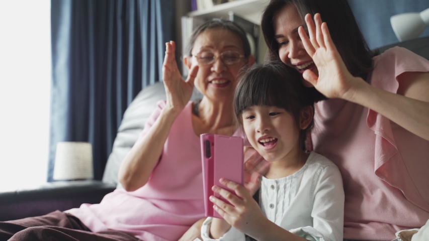 Asian family kid, mother, grandmother talking in video conference by smartphone together in living room at home with happiness and smile. Happy activity technology lifestyle mobile phone use concept. | Shutterstock HD Video #1053791600