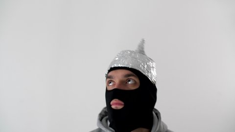 Portrait of a white frightened  man in a black balaclava and a tinfoil hat waved off the 5G waves. Thief or criminal in protective foil helmet. 5G tower radiation protection. Riots and marauding. 