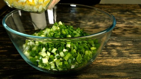 Cooking egg salad with green onions. Sliced scallions and boiled chicken eggs, dill and salt are poured into glass transparent bowl. Close-up.