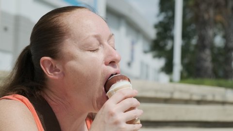 Portrait of happy woman eating ice cream outdoors on sunny day.