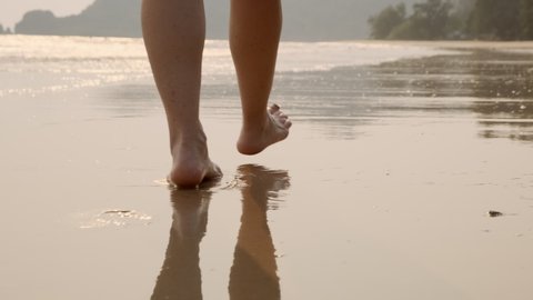 Woman feet walking barefoot on sandy beach of sea.