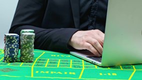 cropped view of player pulling poker chips and using laptop