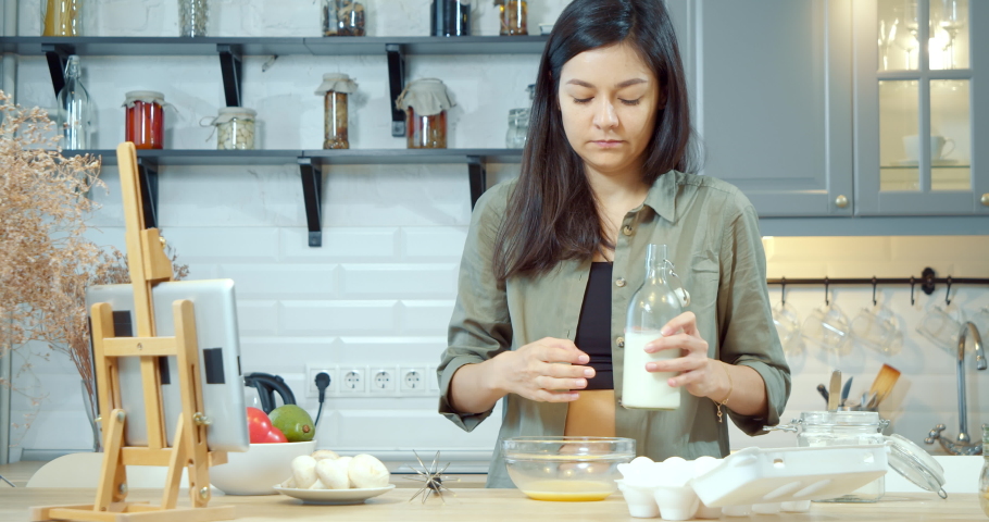 Young attractive woman mixing milk and eggs cooking omelet or pancake dough in the kitchen