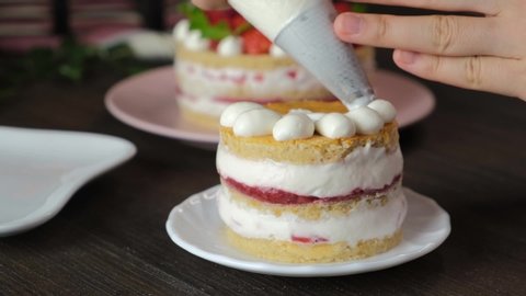 pastry chef decorating strawberry shortcake. woman hand piping cream on cake.