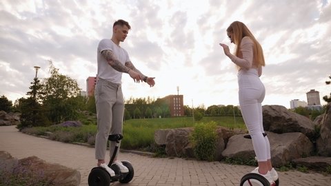 Teenagers ride gyroscuters in a beautiful city Park, a guy helps a girl keep her balance. A young active beautiful girl is learning to ride a self-balancing scooter.