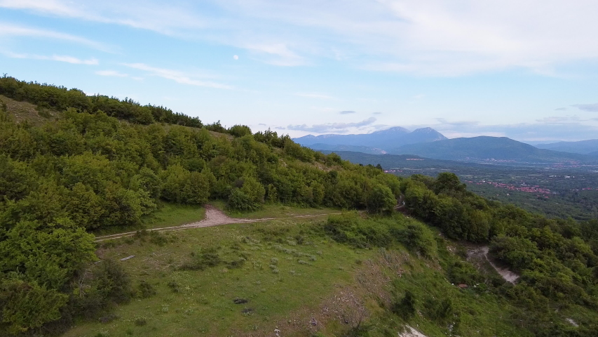 Panoramic view of hill with green trees and city at the back and moon on the sky on day. Aerial drone view 