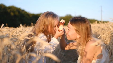 Mother with daughter eat a muffin for a walk in a wheat field. Mom and daughter have fun outdoors in the summer.
