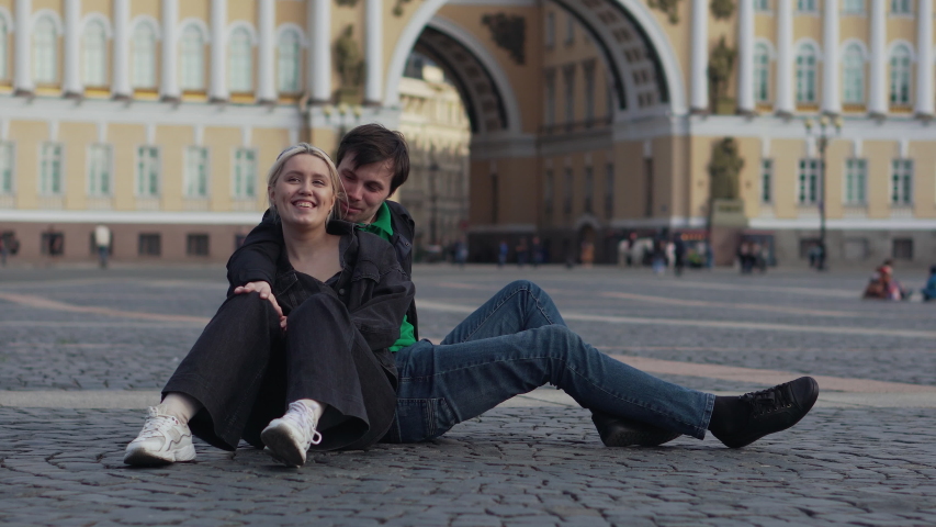 Young beautiful couple in love kisses and have fun outdoors on a warm summer day. A girl and a guy are hugging in a public place.