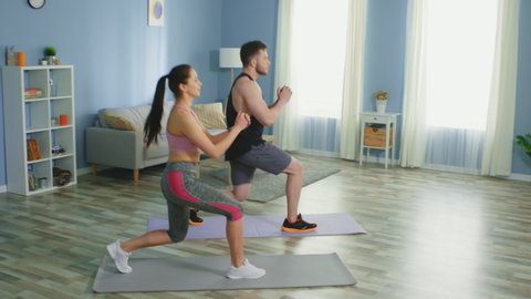 Active couple, man and woman in sport outfits, practice sport at home, doing forward lunges, strengthening their legs, maintain healthy lifestyle, slow motion.