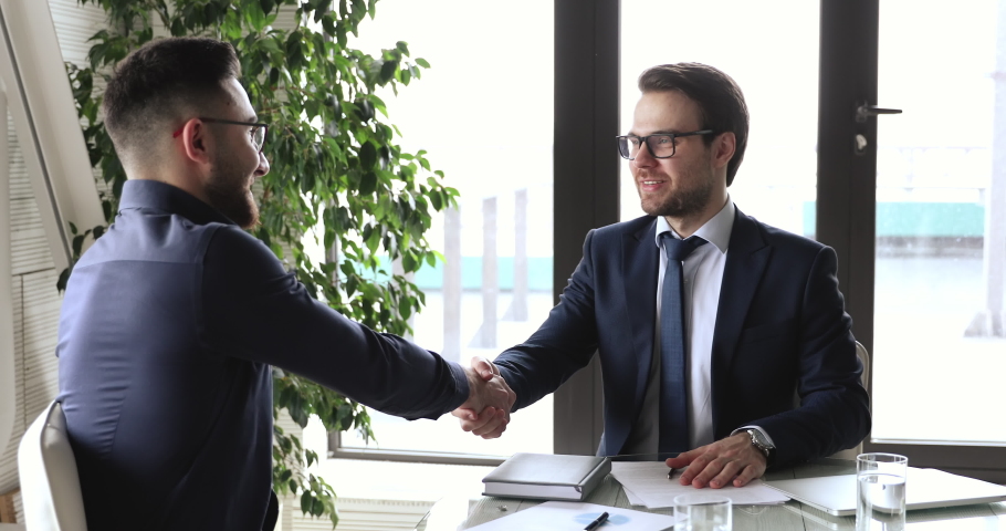Confident caucasian businessman handshaking male arab eastern partner at office meeting. Two multiethnic professional executives shake hands establishing partnership, investment agreement concept. | Shutterstock HD Video #1053812264