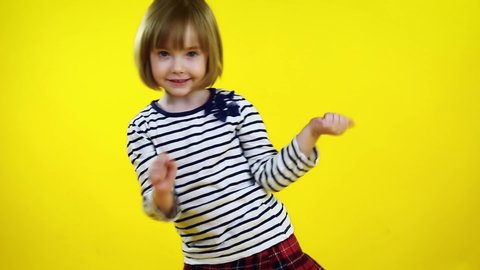 Happy little girl dancing over yellow background. Cute blonde child. 