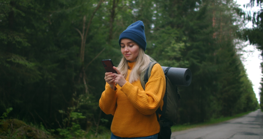 Girl with Backpack Using Smartphone Gps. Woman Hiking In The Forest And Typing Message On Smartphone. Solo female hiker using smart phone. Female hiker takes smart phone pic of mountains and forest. Royalty-Free Stock Footage #1053820181