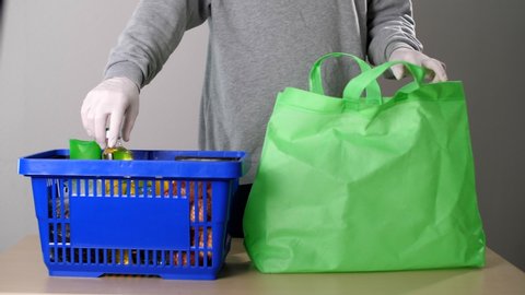 Volunteer pack products. Food delivery services during coronavirus (COVID-19) pandemic for working from home and social distancing. Shopping online. Man folds food in green fabric biodegradable bag. 