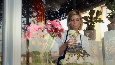 Businesswoman in her own flower shop, preparing bouquet of flowers and holding roses. Pretty girl self-employed in florist store. Confident young woman at work in Milan. Dolly shot