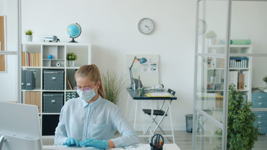 Office workers Caucasian girl and Arab guy are doing elbow high-five at work during quarantine, people are wearing face masks and rubber gloves. | Shutterstock HD Video #1053822416