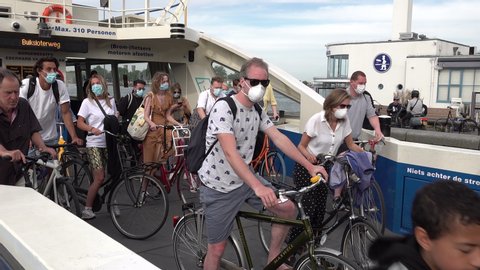 AMSTERDAM, NETHERLANDS – 1 JUNE 2020: People leave ferry boat crossing Het IJ (river) in central Amsterdam, wearing mandatory face masks due to corona virus rules in the Netherlands. Public transport.