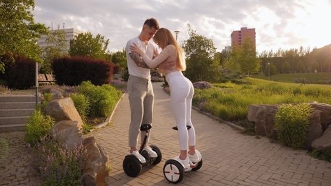 A young sports couple rides a gyro scooter in a beautiful Park in the summer at sunset. Happy man and woman riding on the hoverboard. Active lifestyle. Summer vacation.