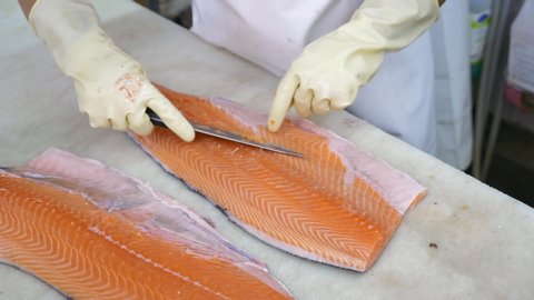Close-up of Worker Hands Cutting and Cleaning Salmon Fillet by Big Chopping Knife in Grocery Store. Clean and Cut Process of Fresh Fish in Supermarket